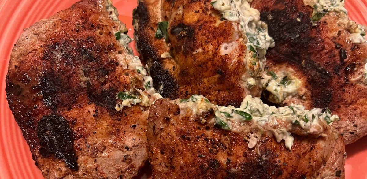 Stuffed pork chops grilling over a wood fire on a fire pit grate
