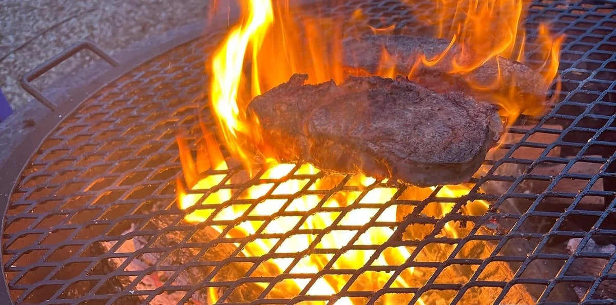 Cajun seasoned ribeye steak searing on a fire pit cooking grate