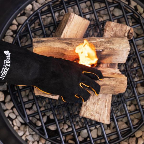 Gloved hand adjusting logs inside a fire pit