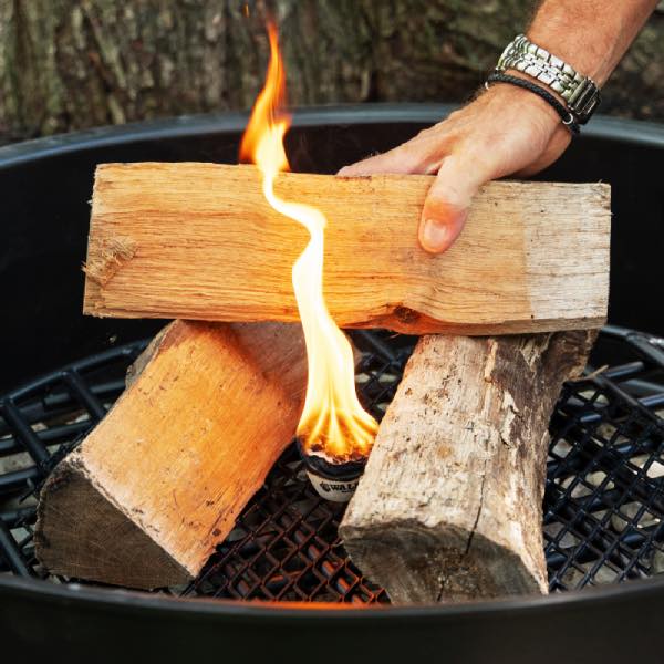 Hand placing a log on top of a fire inside an outdoor fire pit