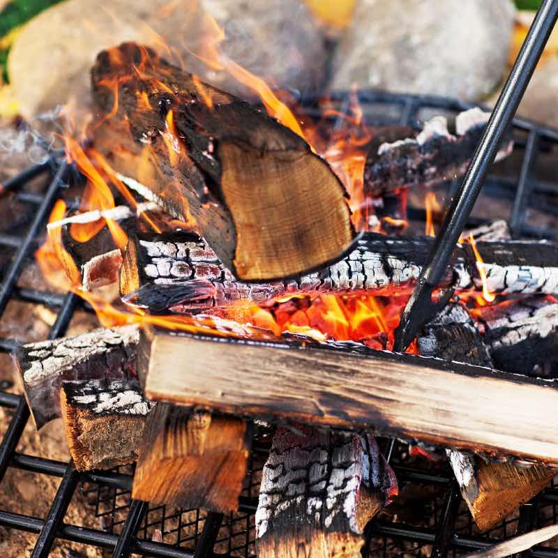 Stacked firewood burning over the thick gridded steel fire grate with hot ember base.