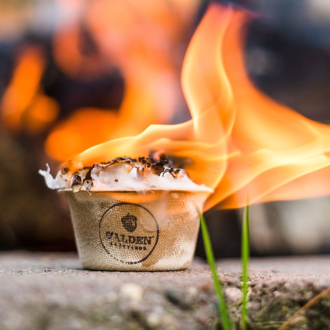 A Walden Sure-Fire starter cup burning with a tall flame at the edge of a fire pit