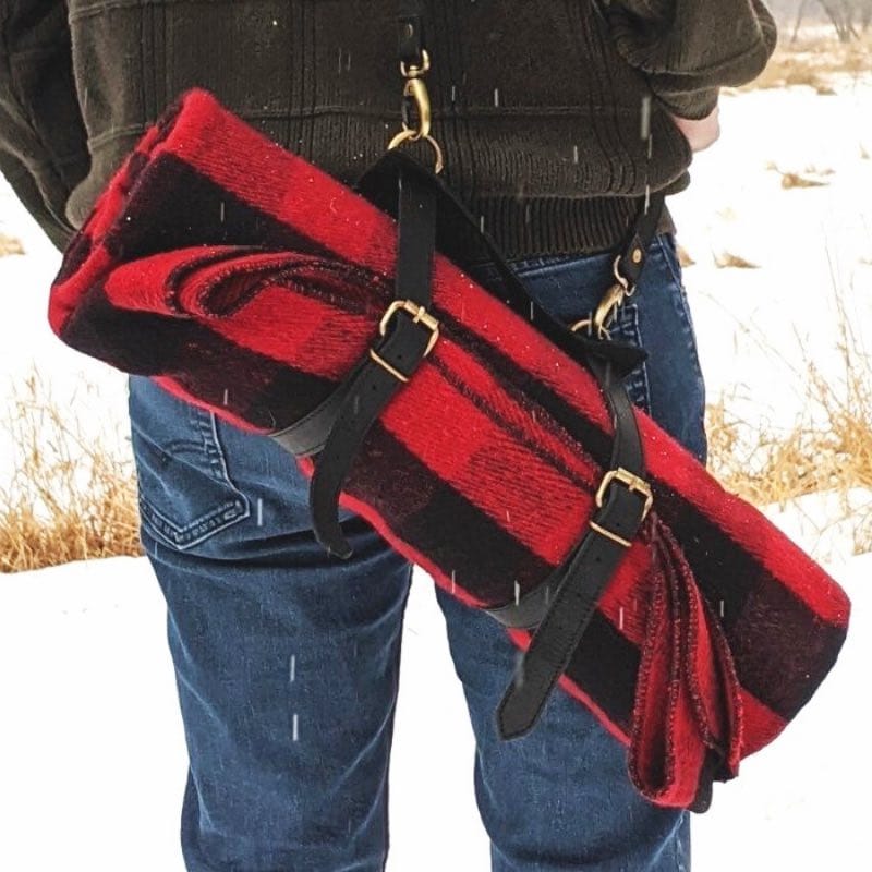 Man carrying the Walden wool blanket on his shoulder by a leather strap as the snow is falling.